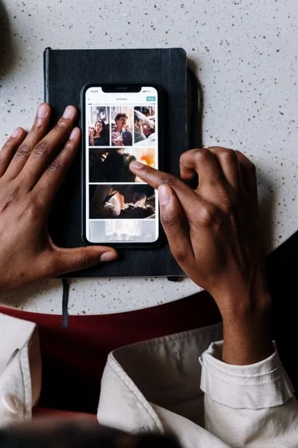 Hand holding smartphone displaying digital wallet app interface, blurred monitor in background.